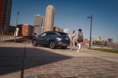 Dos personas conversan mientras caminan por una callle con un Hyundai aparcado detrás.