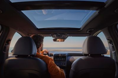 Interior of the Hyundai Tucson Hybrid compact SUV standing at a beach with glass roof ceiling  