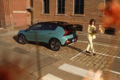 Woman in yellow walking away from the parked Hyundai BAYON compact crossover SUV.