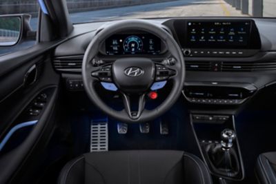 Cockpit eines Hyundai i20 N mit Lenkrad, Bedienelementen, Navigations-Touchscreen, Sportpedalen und Schaltknauf.