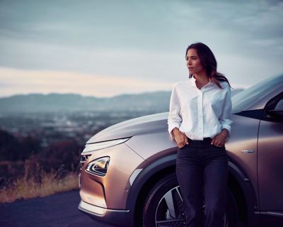 A woman standing before the all-new Hyundai Nexo before a city panorama.