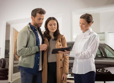 Uomo e donna sorridenti in piedi che guardano lo schermo di un tablet presso un concessionario Hyundai