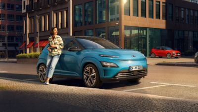 A woman leaning on a Hyundai Kona electric SUV in a city