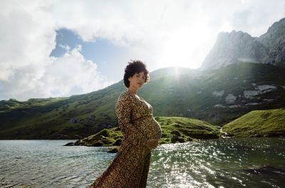 Une femme enceinte tient son ventre devant un lac de montagne.