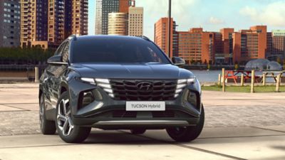 The all-new Hyundai Tucson compact SUV pictured from the front parked near a waterfront skyline.