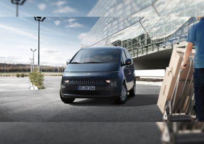 The Hyundai STARIA Van in front of a futuristic-looking building. 