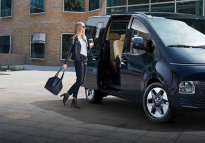 A woman holding a cup of coffee getting into the all-new Hyundai STARIA.
