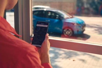 Una mujer mira la aplicación Hyundai Bluelink® en su smartphone con su coche aparcado en la calle.