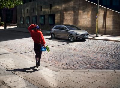 Femme marchant vers Hyundai i30 stationnée dans la rue.