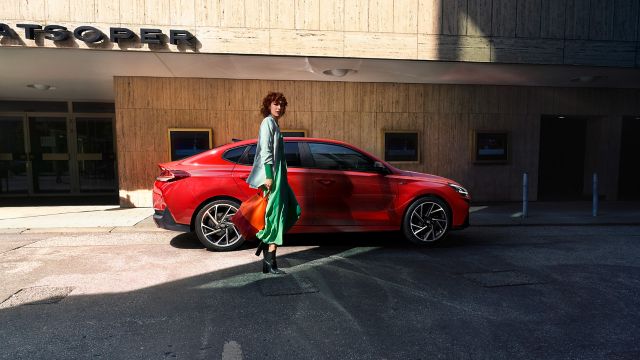 Mladá žena stojící u zaparkovaného modelu Hyundai i30 Fastback.