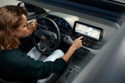 Žena za volantem svého modelu Hyundai i30 používá dotykovou obrazovku.