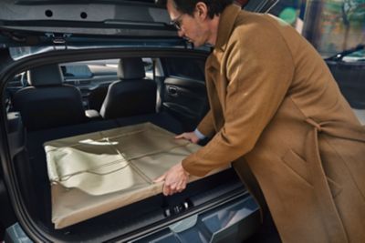 A man in a brown coat putting a wrapped painting into the all-new Hyundai i20's boot