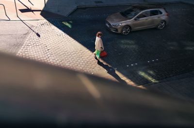 Žena kráčí směrem k Hyundai i30 s červenou taškou v ruce.