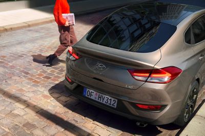 Woman approaching her Hyundai i30 Fastback on the driver's side.