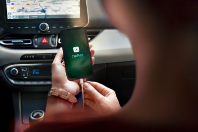 Vrouw kijkt naar haar iPhone met het Apple CarPlay-pictogram, een Hyundai-aanraakscherm op de achtergrond.