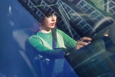 Young woman sitting in her Hyundai i30 Fastback, hands on the steering wheel.