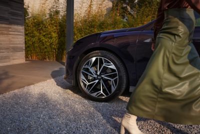 Lato di Hyundai IONIQ 6 con una sola ruota visibile e una persona con una gonna verde cammina accanto all'auto