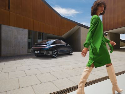 Hyundai IONIQ 6 100% elettrica parcheggiata in un luogo pubblico e donna con abito verde che cammina