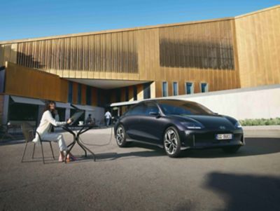 Hyundai IONIQ 6 100% elettrica parcheggiata davanti a un edificio con una donna seduta accanto