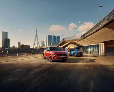 The all-new Hyundai Kona N Line in red driving over a bridge next to a city.