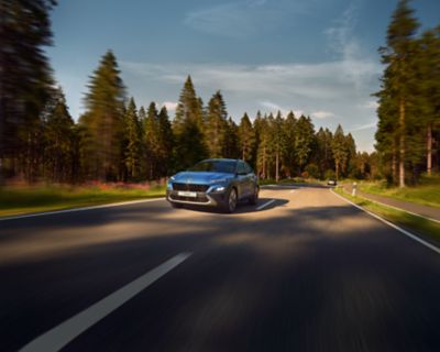 The new Hyundai Kona from the front in Surfy Blue driving down a forest road.