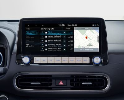Immagine dello schermo del sistema di navigazione da 10,25” di Nuova Hyundai Kona Electric che mostra informazioni sui parcheggi lungo la strada e in aree dedicate.
