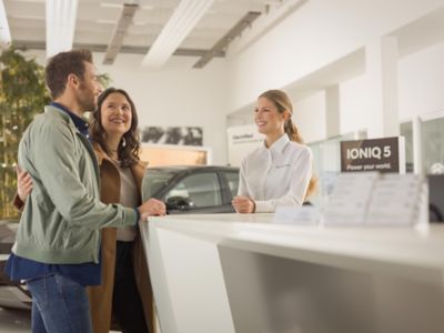 Smiling man and woman standing at an info desk talking to a Hyundai dealer representative.