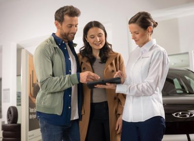 A Hyundai dealer with a tablet computer showing details about the Hyundai KONA to a man and a woman.