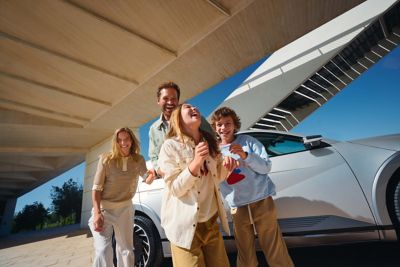 Une famille de quatre personnes heureuse se tient à côté du véhicule électrique Hyundai IONIQ 5.