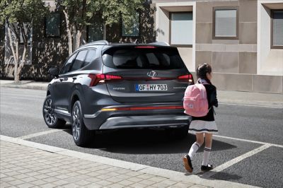 The new Hyundai Santa Fe 7 seat SUV from the back, with a school girl crossing behind the car.
