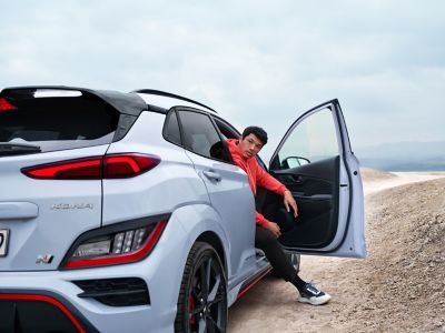 Un joven con ropa deportiva saliendo por la puerta del pasajero del Hyundai KONA N, visto desde atrás