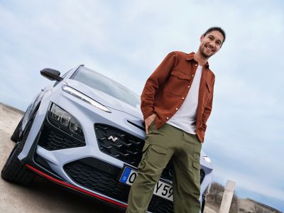 Un jeune homme adossé contre le capot du SUV sportif Hyundai KONA N, souriant avec assurance.