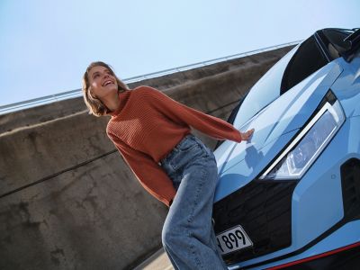 A woman sitting on the trunk of the Hyundai i20 N in performance blue.