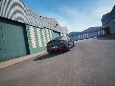 the new Hyundai i30 N Fastback driving in an industrial scenery from the rear.