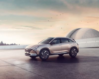 The all-new Hyundai Nexo, shown from the side, standing before a futuristic building at sunset.
