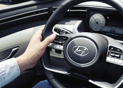 Die Hand eines Mannes drückt eine Funktionstaste am Lenkrad eines Hyundai TUCSON.