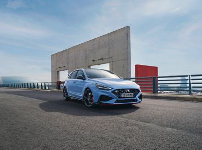 Vista frontale di Nuova Hyundai i30 N in Performance Blu parcheggiata accanto a un edificio industriale
