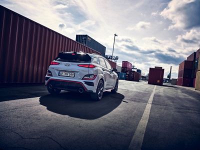 Vue arrière du SUV sportif Hyundai KONA N évoluant à toute vitesse entre les conteneurs d’un site industriel.