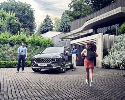 The Hyundai Santa Fe 7 seat SUV in grey parked in front of a luxurious family house.
