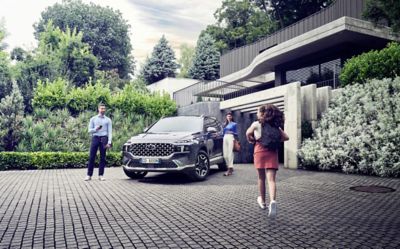 Nuova Hyundai Santa Fe Hybrid parcheggiata di fronte ad una casa con una famiglia in procinto di entrare in auto