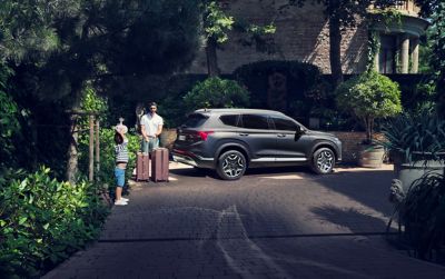 Famiglia con valige accanto a Hyundai Santa Fe Plug-in Hybrid