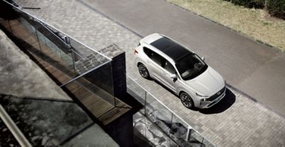 The new Santa Fe 7 seat SUV in white from above parked in front of a house.