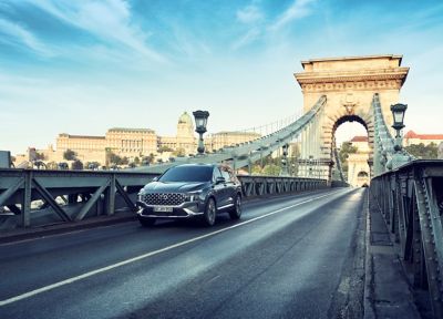 The SANTA FE 7 seat SUV in grey driving over a city bridge.