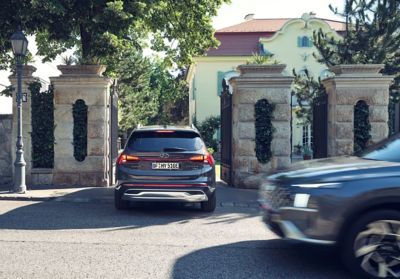 The new Hyundai Santa Fe Plug-in Hybrid 7 seat SUV driving through an entrance gate of a house.