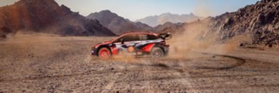 The Hyundai i20 N WRC rally race car drifting in circles in the desert.