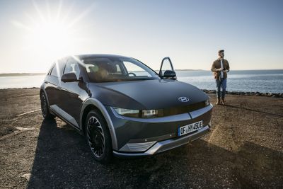 The Hyundai IONIQ 5 electric vehicle at the beach with a man standing next to it.