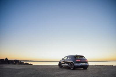 Ein IONIQ 5 steht auf einem Parkplatz an einer Küste mit Ausblick auf den Sonnenuntergang.