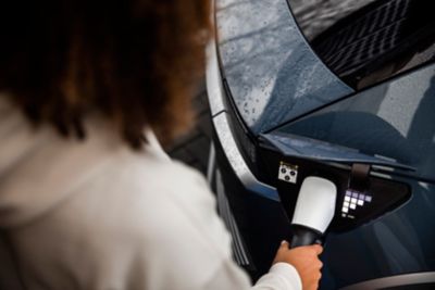 Woman interacting with her phone while her Hyundai charges in the background.