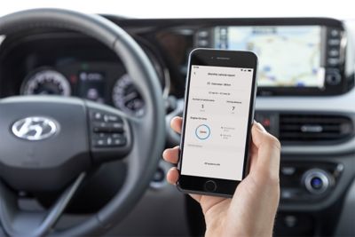 Eine Hand hält im Innern eines Hyundai ein Smartphone, auf dessen Bildschirm die Bluelink App zu sehen ist.