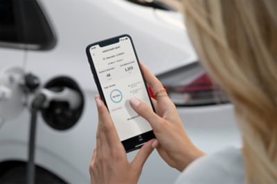 Femme consultant le statut de sa Hyundai IONIQ sur son téléphone tout en rechargeant sa voiture.